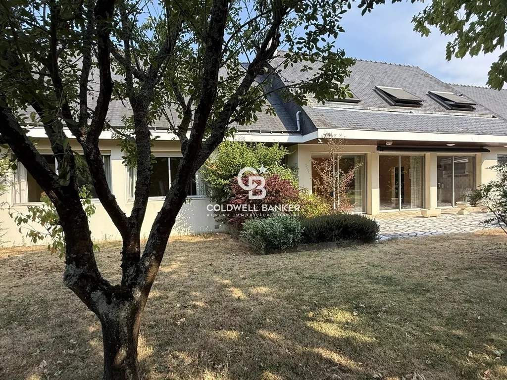 Vue extérieure sur la maison et sa terrasse en pierre, entourée d'un jardin arboré à Laval.