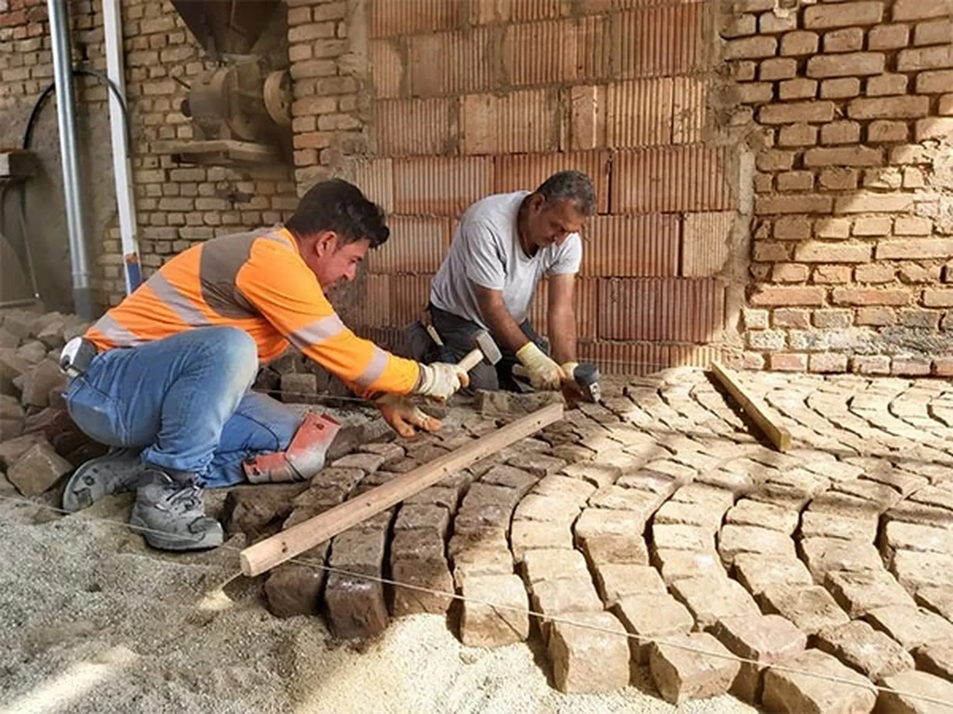 Artisans pavéiers posant des pavés en pierre naturelle en éventail sur un lit de sable.