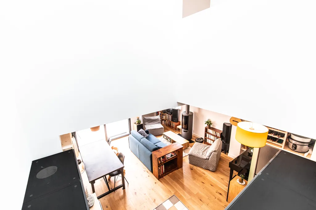 Perspective sur le salon et la cuisine depuis la mezzanine  AKIKO ARCHITECTURE – Bègles – Transformation intérieure La mezzanine offre une lecture d’ensemble du cœur de la maison : un salon convivial baigné de lumière naturelle, articulé autour d’un patio