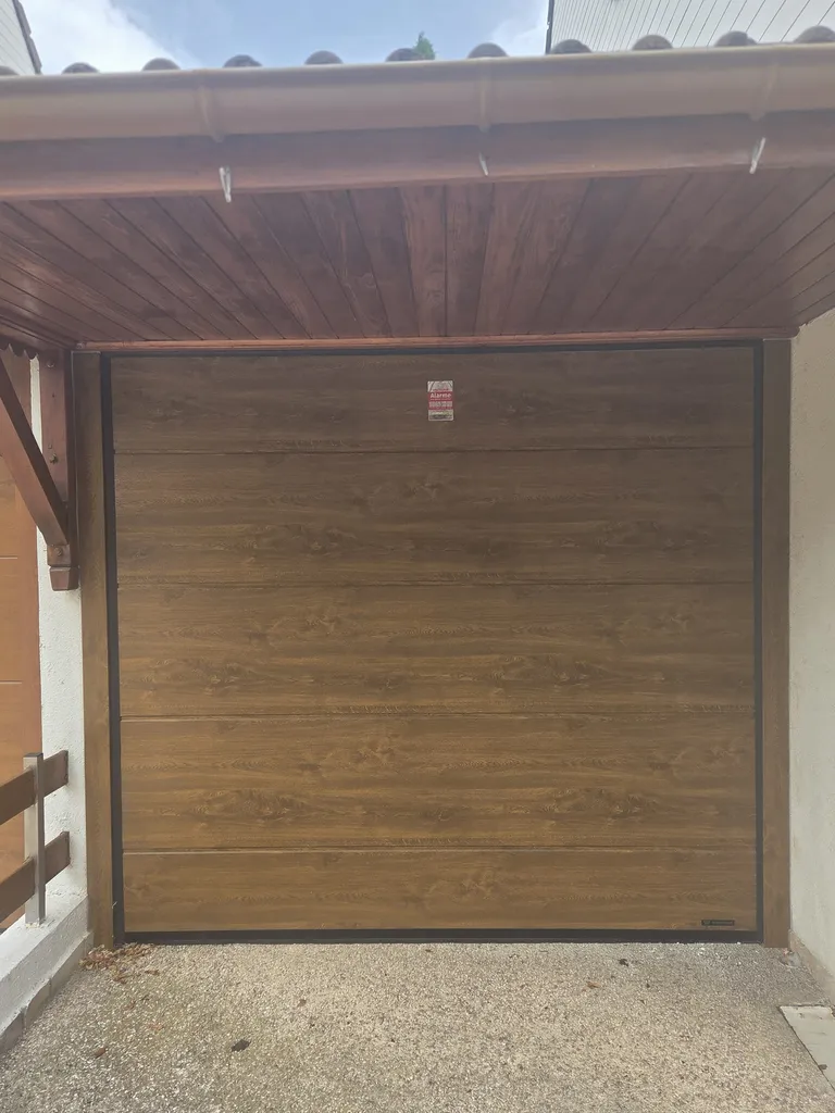 Installation à Sassenage d’une porte de garage sectionnelle motorisée sur mesure avec panneaux isolés en finition chêne doré