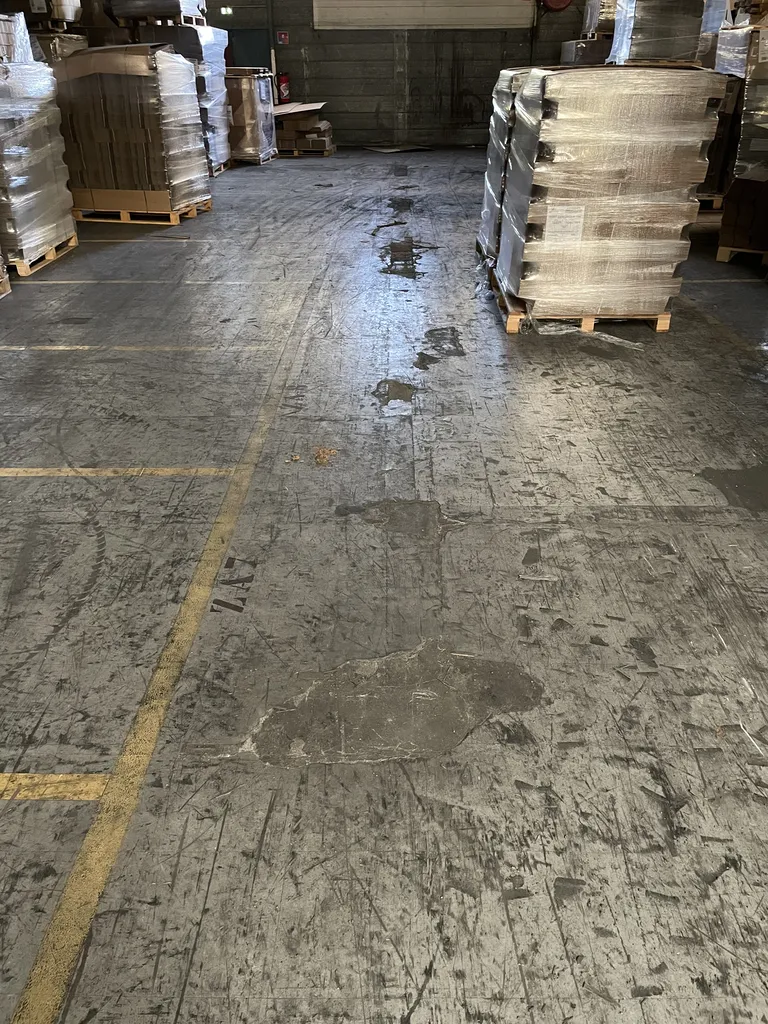 Sol en béton avant travaux de réparation dans un entrepôt à Belleville-en-Beaujolais (Rhône – 69), présentant des dégradations et fissurations