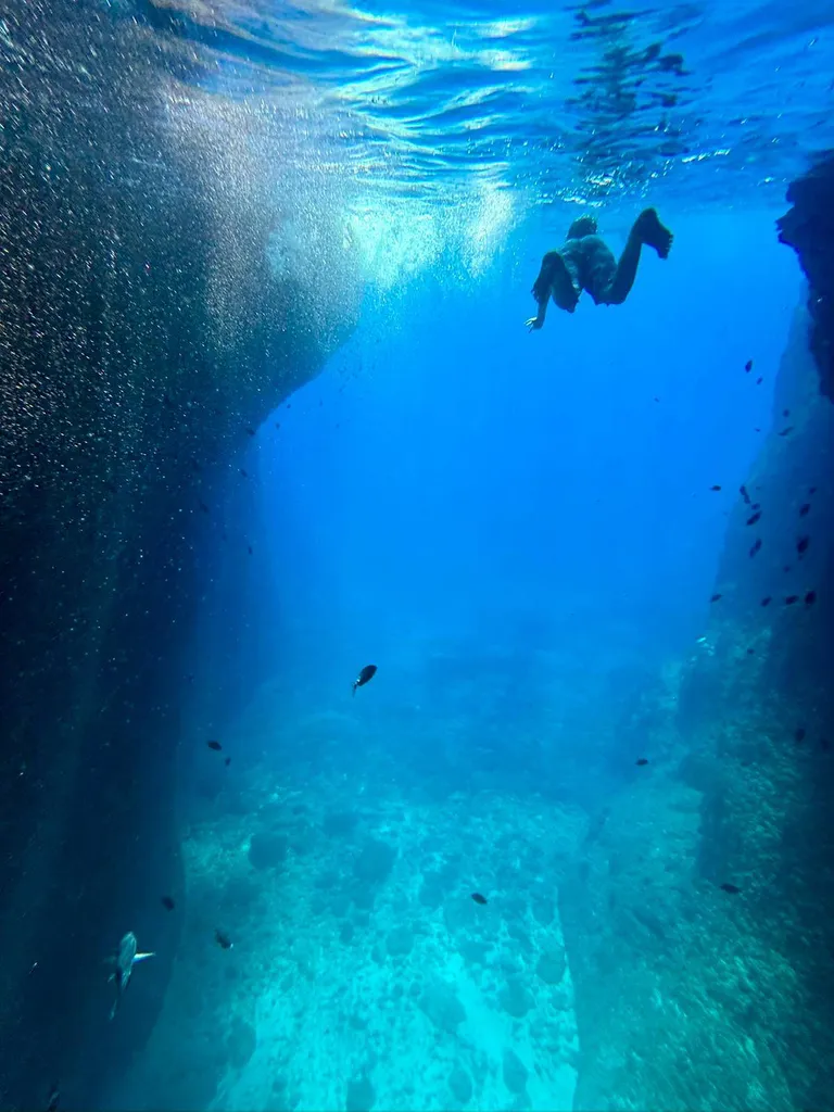 Explorateur nageant vers la grotte semi-immergée de l'Oule, entourée de falaises imposantes