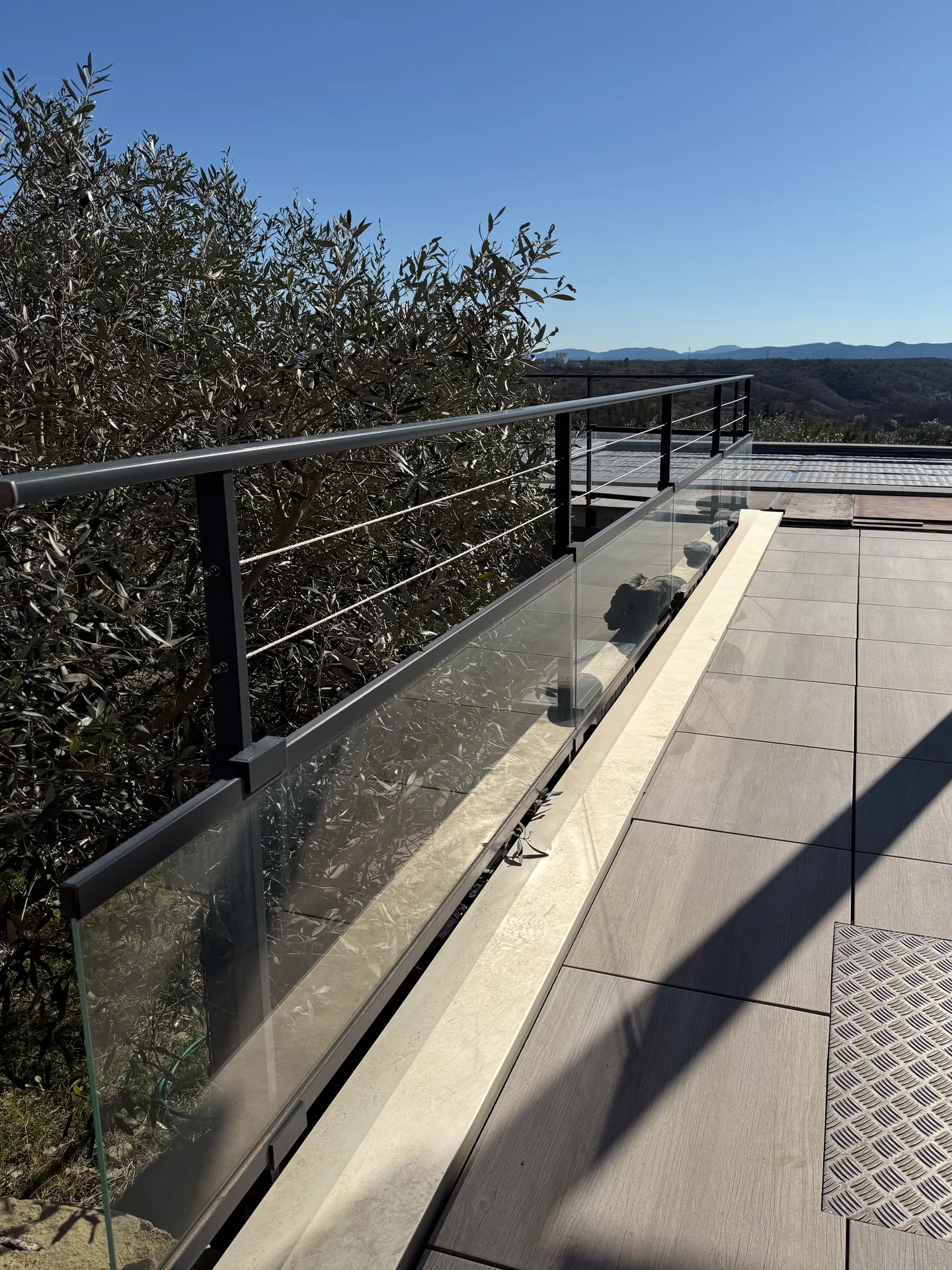 La finesse d’un garde-corps mêlant verre, câbles inox et aluminium pour ouvrir la terrasse sur le paysage