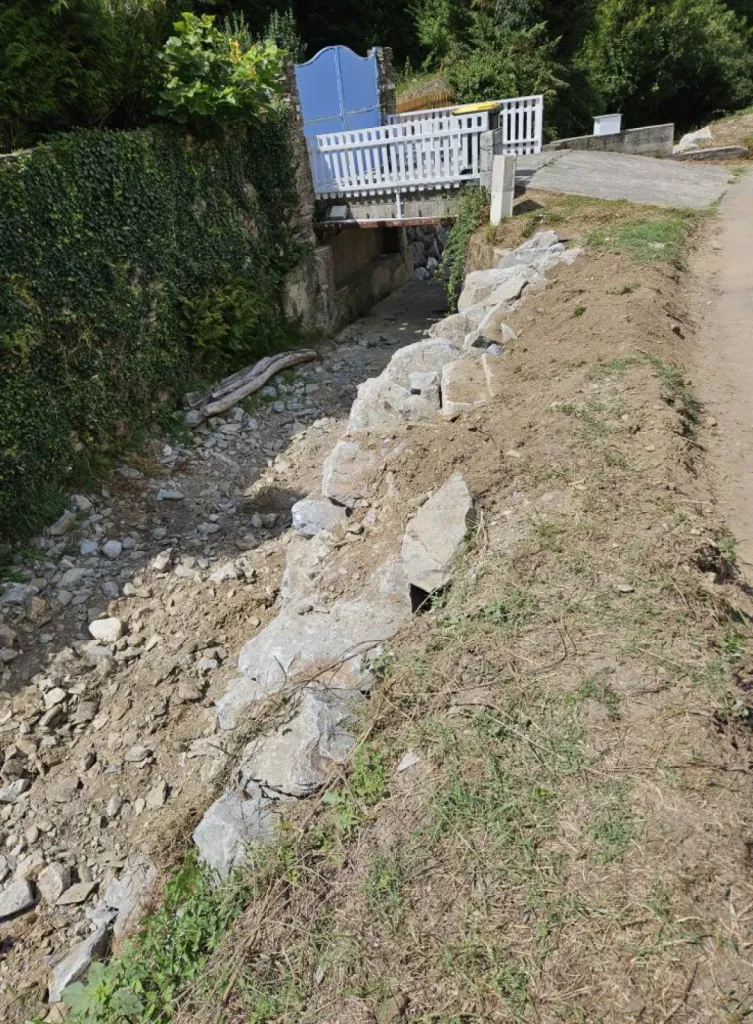 Entreprise de terrassement dans l'Ain pour Réalisation d'un enrochement brute avec grosses pierres pour soutenir le mur du fossé à l'entrée d'une maison à Saint-Genis-Pouilly