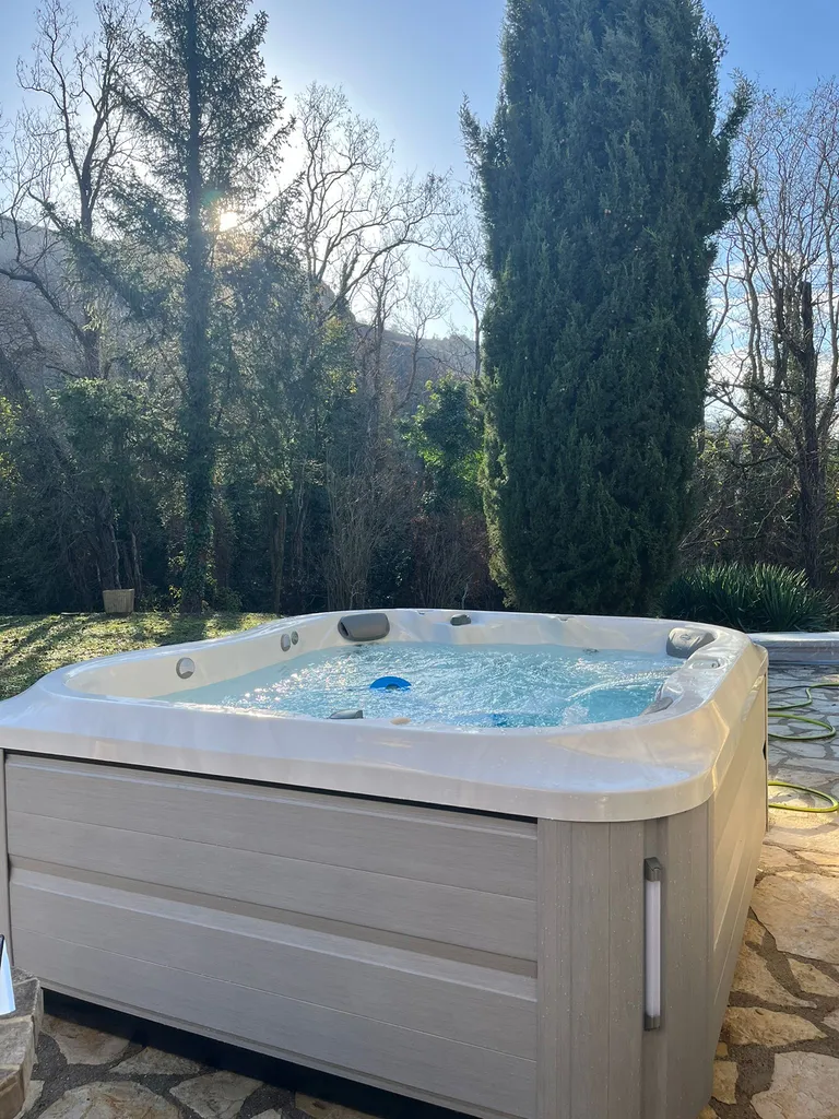 Jacuzzi J-355 sur une terrasse en dalle de pierre dans un environnement de sapins 
