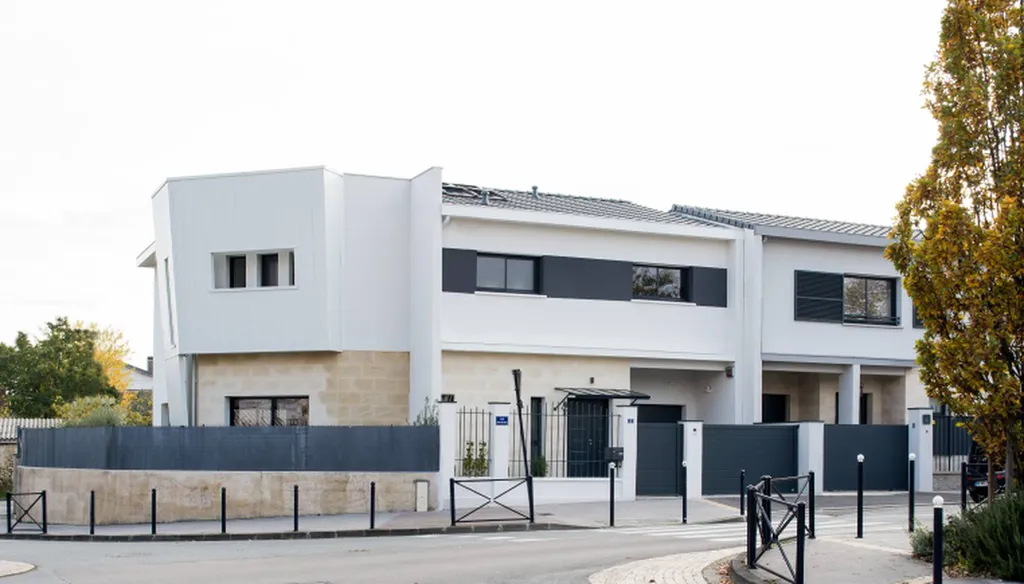 Maison contemporaine à étage avec façade en pierre blonde, enduit blanc et menuiseries gris anthracite, construite par Maisons Héraud en Gironde.