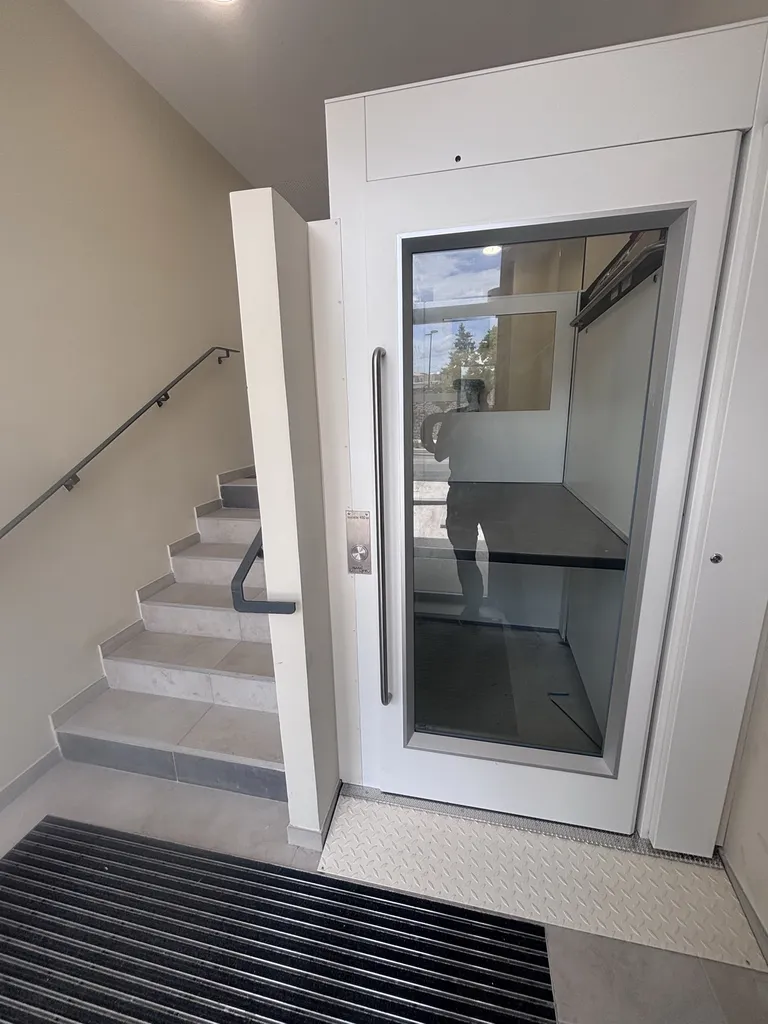 Idéalement situé dans le hall l'élévateur vertical Namilift PL400 permet aux personnes en perte d'autonomie de franchir ce dénivelé dans cet immeuble neuf à Trets près de Marseille