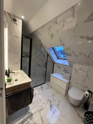Transformation complète d’un espace sous combles en salle de bain moderne avec carrelage effet marbre et douche vitrée à Paris (75)