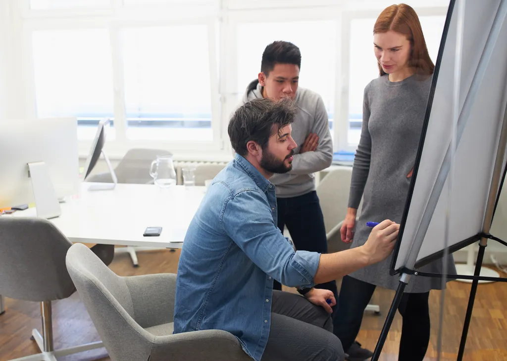 Trois managers travaillent ensemble autour d’un paperboard
