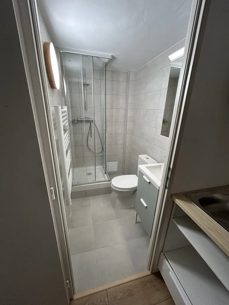 La nouvelle salle de bain finie et fonctionnelle du studio, optimisée avec WC, faïence murale contemporaine, mitigeur et paroi de douche vitrée.
