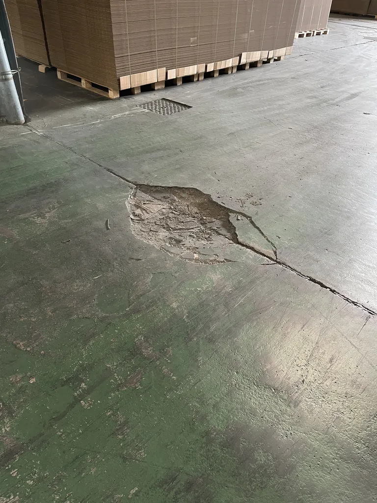 Sol en béton avant réparation dans un entrepôt à Belleville-en-Beaujolais (Rhône – 69), avec fissures et nids de poule causés par les contraintes d’exploitation