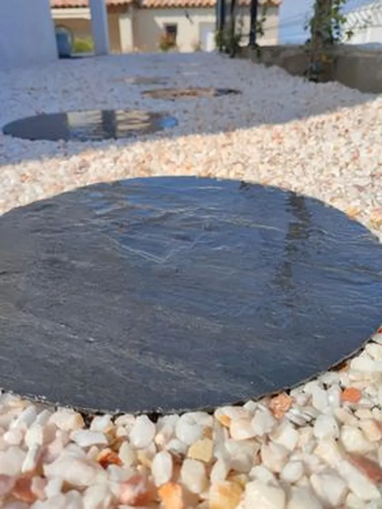 Dalle ronde en ardoise sombre posée au milieu de galets clairs, pour un projet à Ajaccio en Corse.