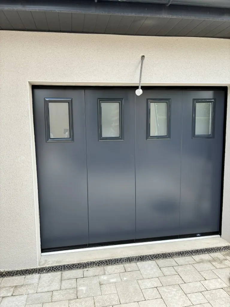 Installation d'une porte de garage à déplacement latéral motorisée en acier isolé laqué avec hublots à Misérieux