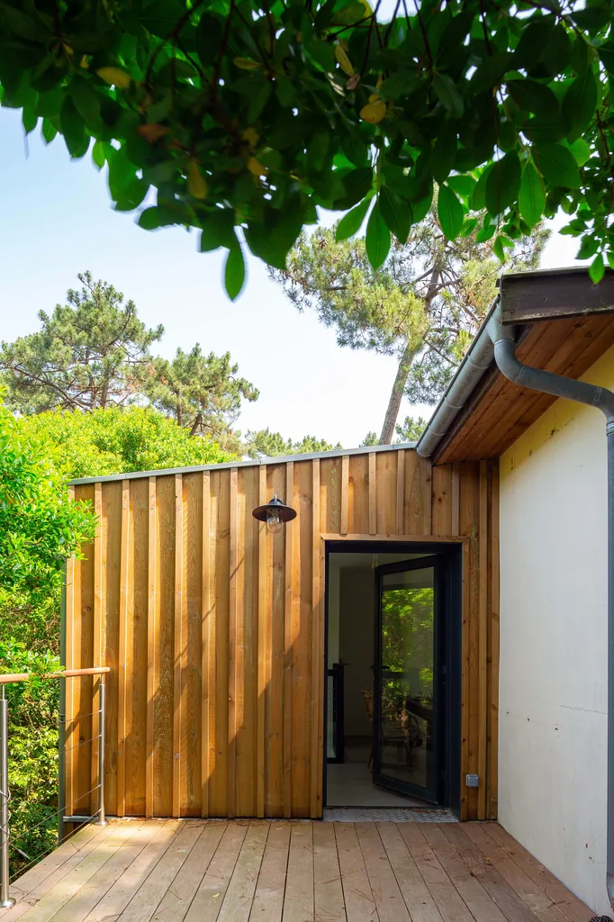 Façade arrière et terrasse surélevée  AKIKO ARCHITECTURE — Piraillan, Cap-Ferret — intervention bois & restructuration En façade arrière, la terrasse sur pilotis s’avance au-dessus du sol naturel et crée un nouvel espace extérieur connecté à l’étage. Le v
