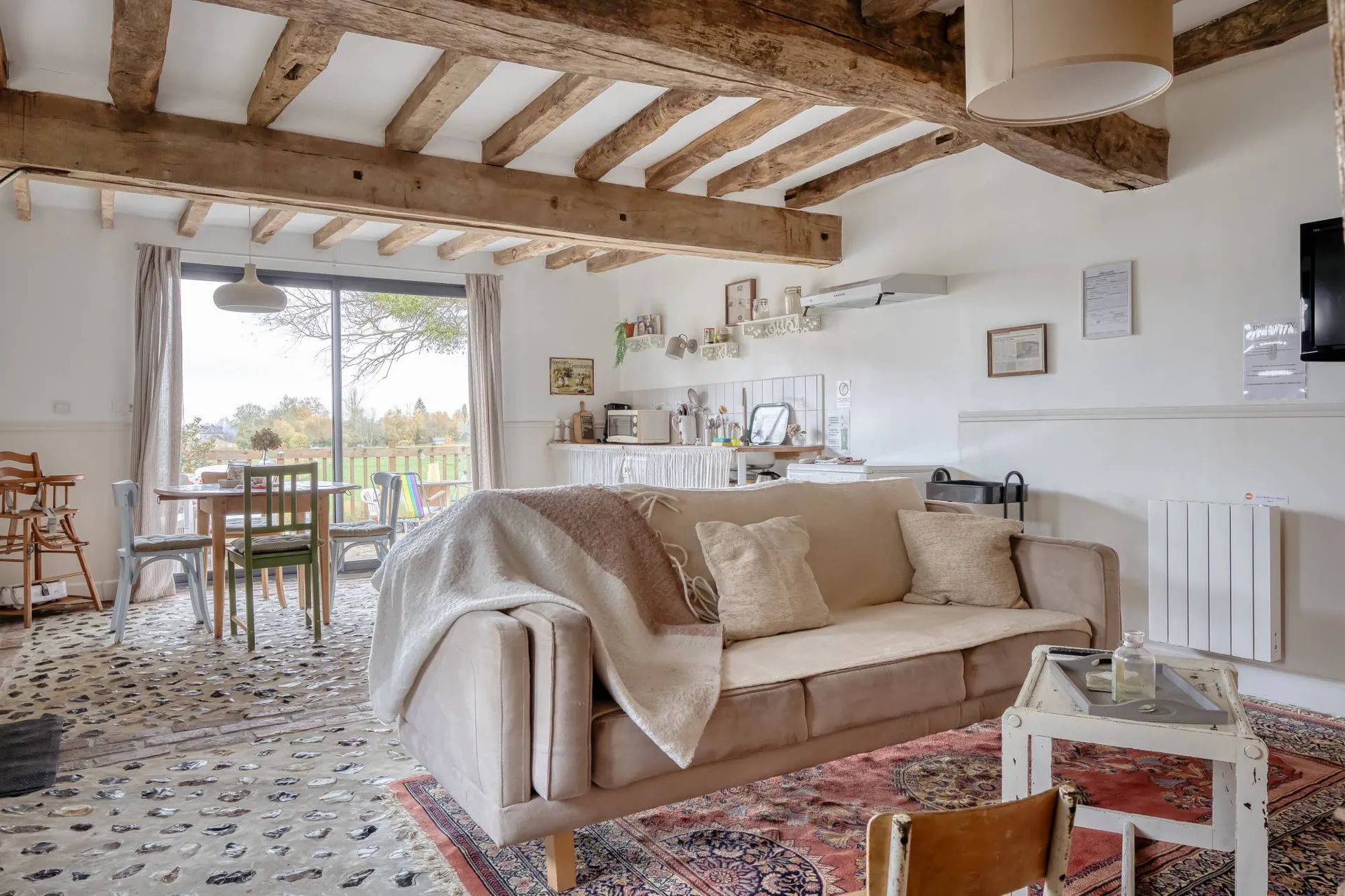 Vends séjour du gîte avec grande baie vitrée donnant sur la terrasse et le jardin arboré.