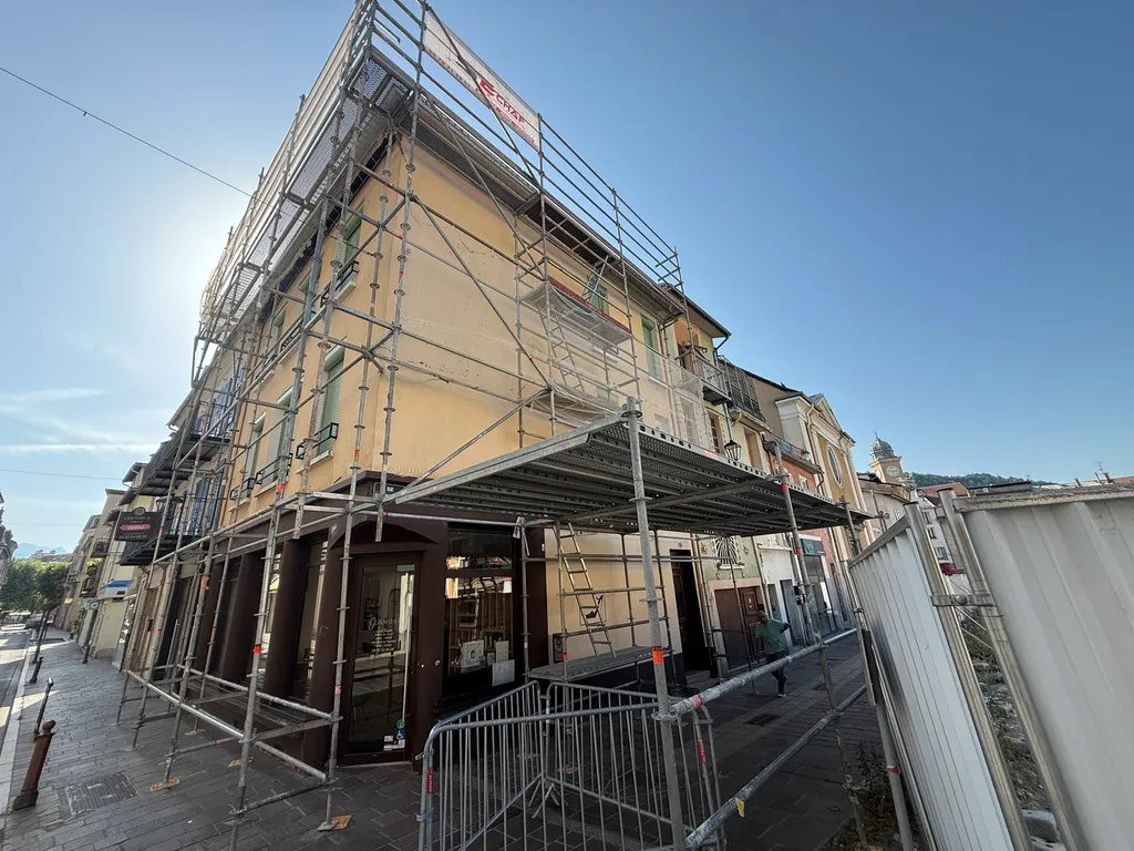 Échafaudage multidirectionnel Layher installé sur un immeuble d’angle en centre-ville de Gap, avec passage protégé sous structure pour maintenir la circulation au pied du bâtiment pendant les travaux de charpente.