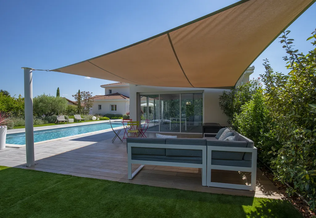Aménagement paysager avec terrasse bois, gazon synthétique et voiles d’ombrage autour d’une piscine à Genas (69740)