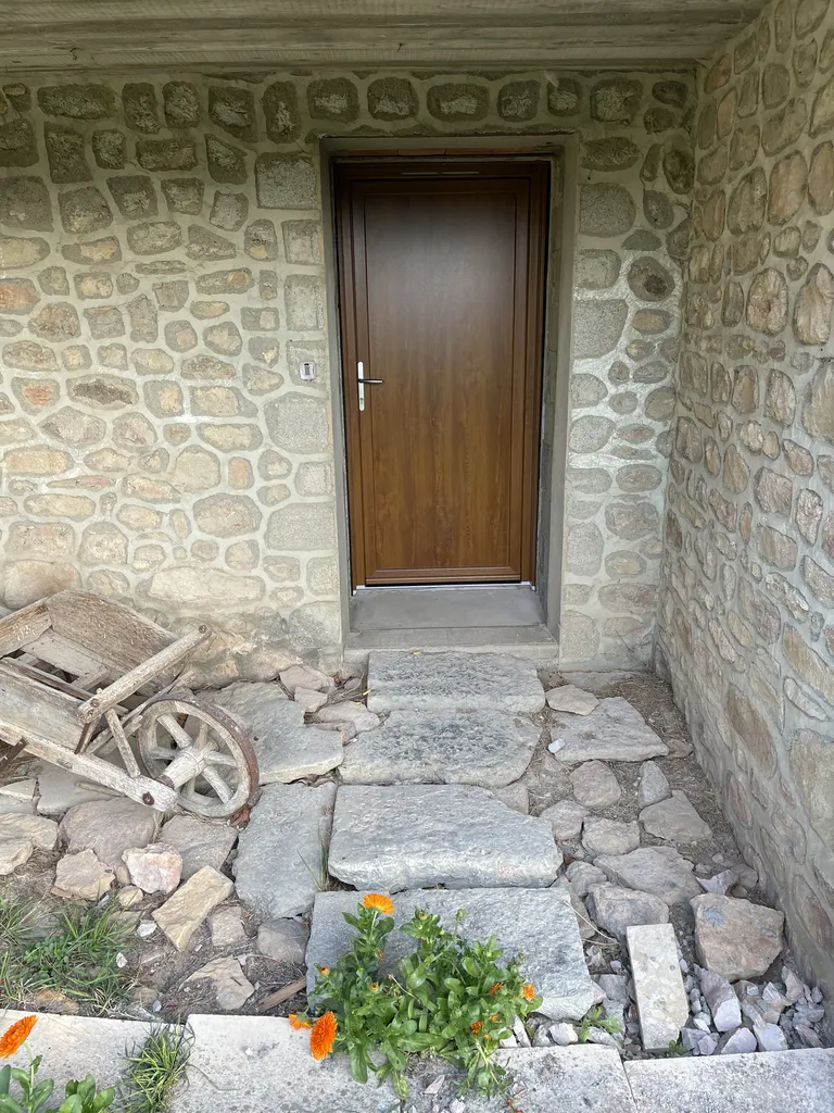 Porte d’entrée en PVC imitation bois parfaitement intégrée à une maison en pierre à Beaujeu (Rhône 69), offrant une excellente performance énergétique tout en respectant le charme du bâti ancien