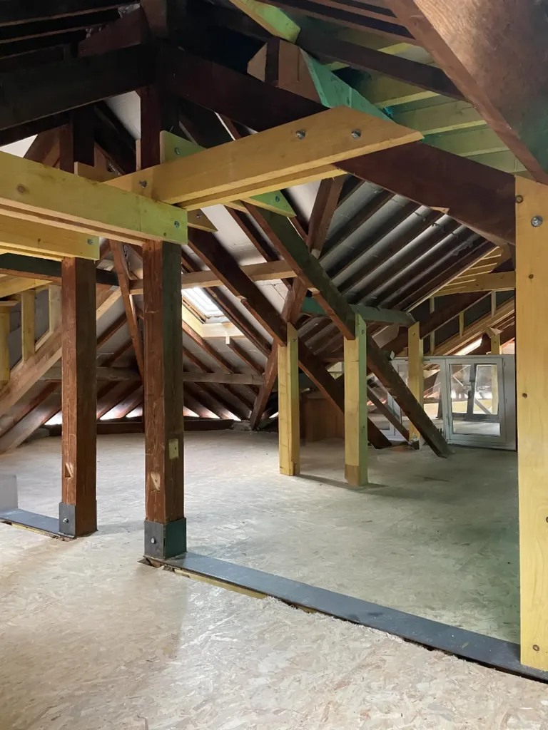 Vue intérieure brute de la surélévation de maison mettant en valeur la structure porteuse et la charpente neuve apparente avant isolation