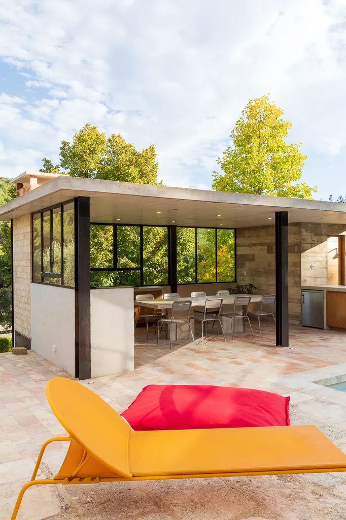 Pool house contemporain ouvert sur piscine avec cuisine extérieure et matériaux naturels en Provence