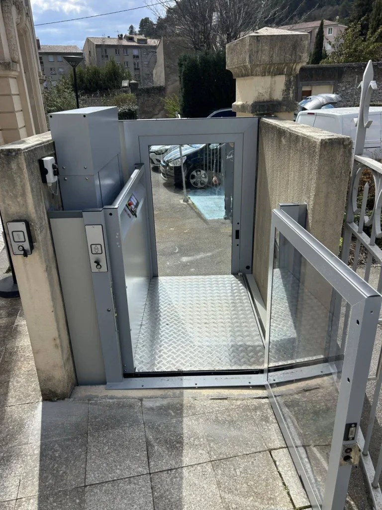 Le passage libre du portillon permet aux personnes en situation de handicap d'accéder facilement à l'étage via cette plateforme verticale en extérieur dans un ERP à Sisteron