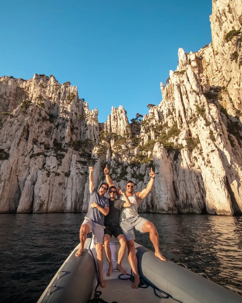 Groupe de jeunes hommes profitant d'une escale baignade dans une anse préservée des Calanques, bateau de L'Eden Boat ancré en arrière-plan