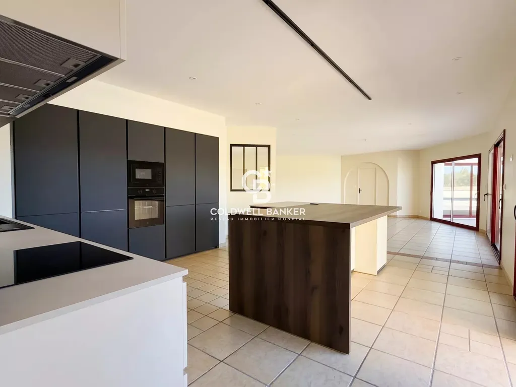Cuisine ouverte avec îlot central, colonnes noires et fours encastrés, dans une maison rénovée à 15 minutes du Mans