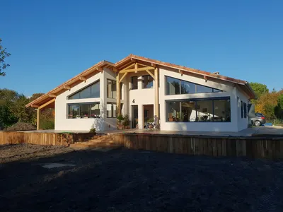 Maison landaise contemporaine conçue par AKIKO ARCHITECTURE à Léon : une façade avant réinterprétée, mêlant charpente bois traditionnelle et grandes ouvertures modernes, imaginée pour s’intégrer harmonieusement au paysage verdoyant des Landes