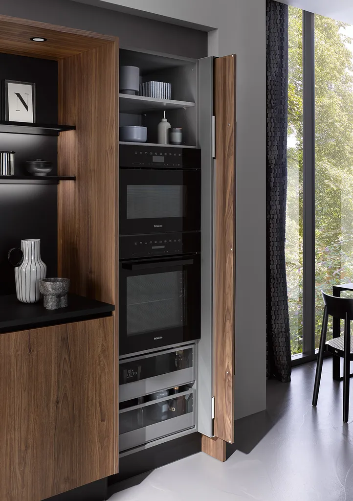 Portes coulissantes pour dissimuler les électroménagers dans une cuisine ou la chaleur du noyer contraste avec le design froid de l'acier