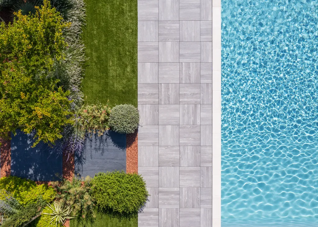 Aménagement paysager avec terrasse bois, gazon synthétique et voiles d’ombrage autour d’une piscine à Genas (69740)