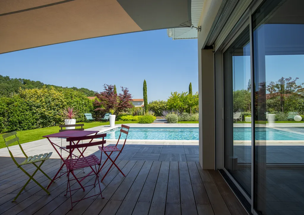Aménagement paysager avec terrasse bois, gazon synthétique et voiles d’ombrage autour d’une piscine à Genas (69740)