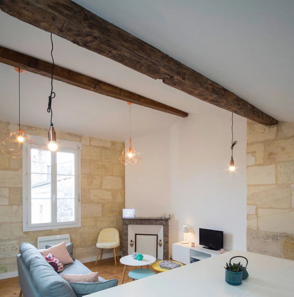 AKIKO ARCHITECTURE – Bordeaux Chartrons — Rénovation & réagencement sous combles Les poutres apparentes ont été mises en valeur par un travail précis sur la lumière : suspensions cuivrées, lignes épurées et tonalités douces viennent moderniser cet apparte