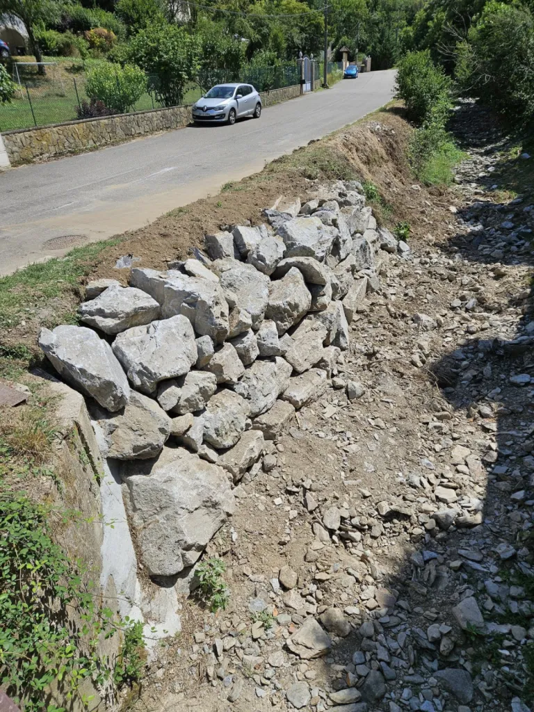 Entreprise de terrassement dans l'Ain pour Réalisation d'un enrochement brute avec grosses pierres pour soutenir le mur du fossé à l'entrée d'une maison à Saint-Genis-Pouilly