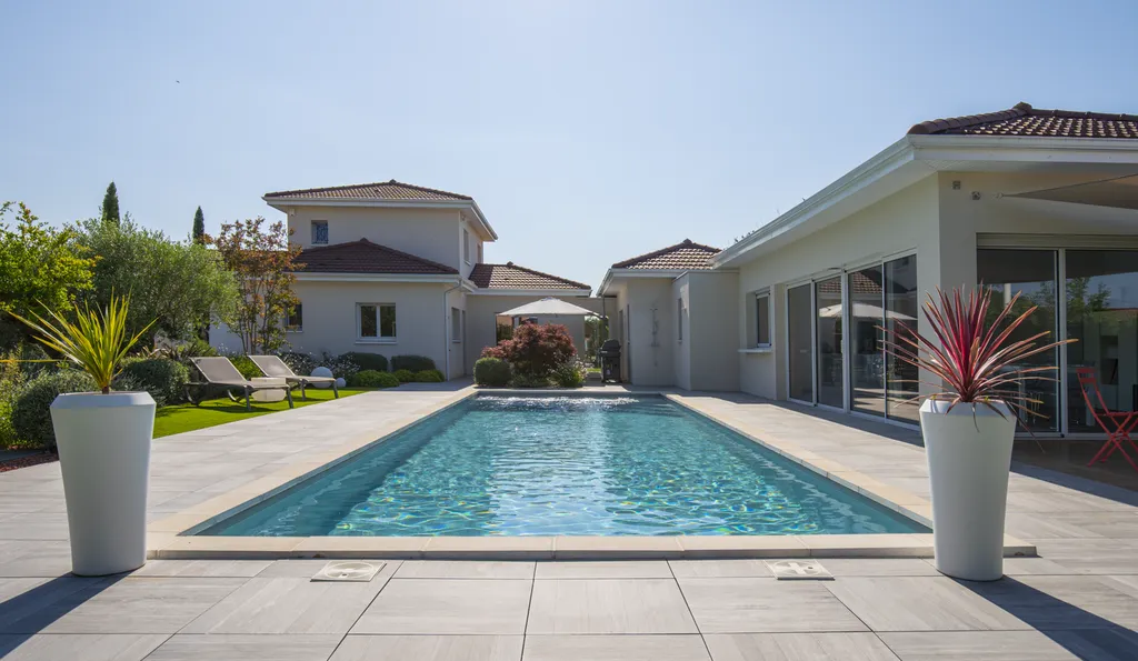 Aménagement paysager avec terrasse bois, gazon synthétique et voiles d’ombrage autour d’une piscine à Genas (69740)