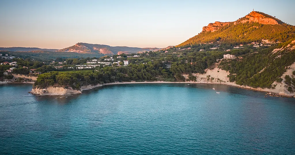 Vue panoramique depuis la mer sur une large baie encadrée de falaises blanches et de collines de garrigue