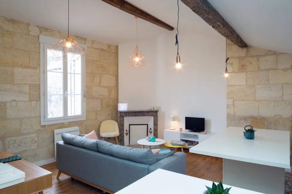 AKIKO ARCHITECTURE – Bordeaux Chartrons — Rénovation & réagencement sous combles Dans ce séjour intégralement repensé, l’agence a révélé la pierre blonde d’origine, conservé les poutres anciennes, et imaginé un espace de vie lumineux articulé autour d’un 