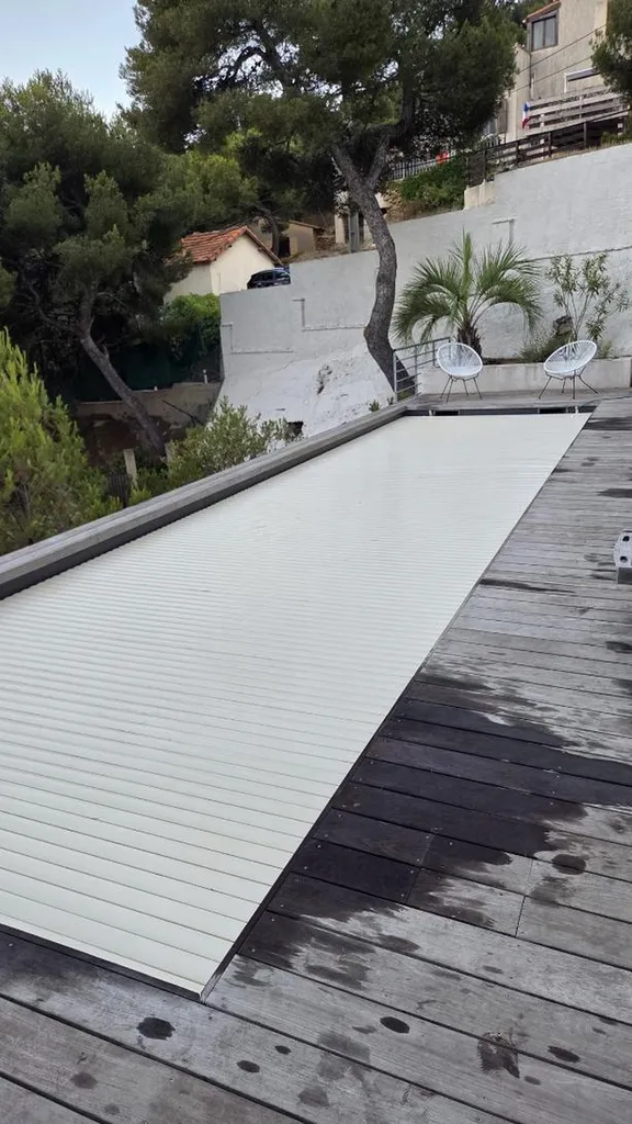 Volet roulant immergé de piscine déroulé sur bassin à Ensuès-la-Redonne : lames PVC crème et terrasse bois