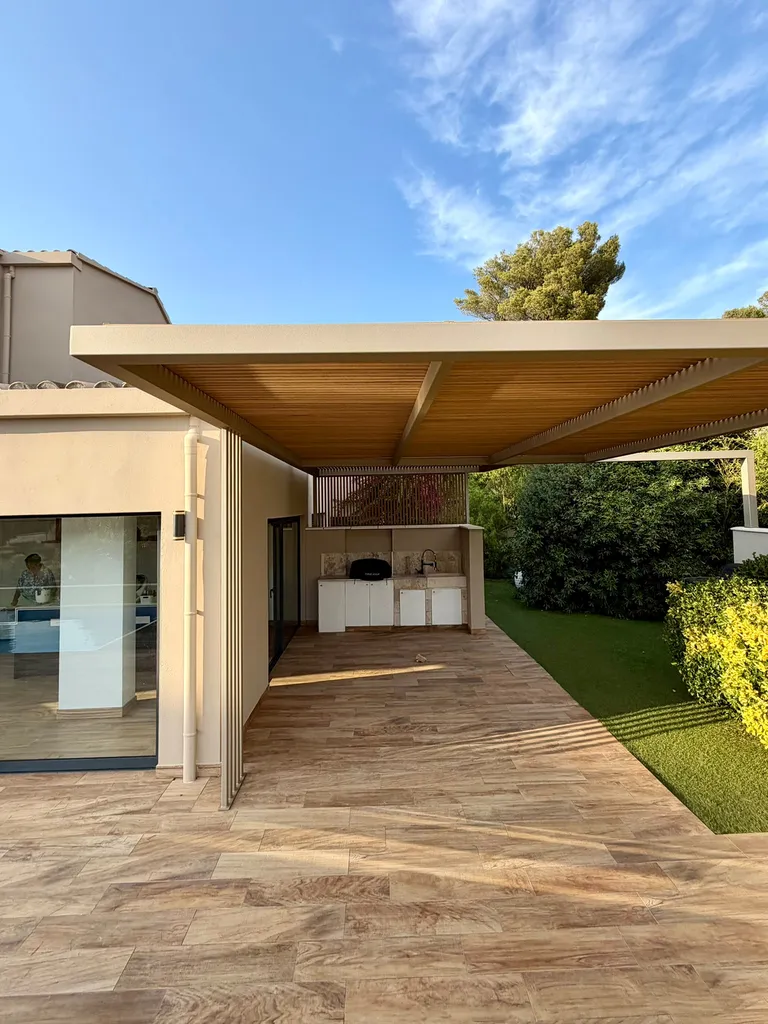 pergola en acier adossée abritant une cuisine d'été sur mesure et son plan de travail