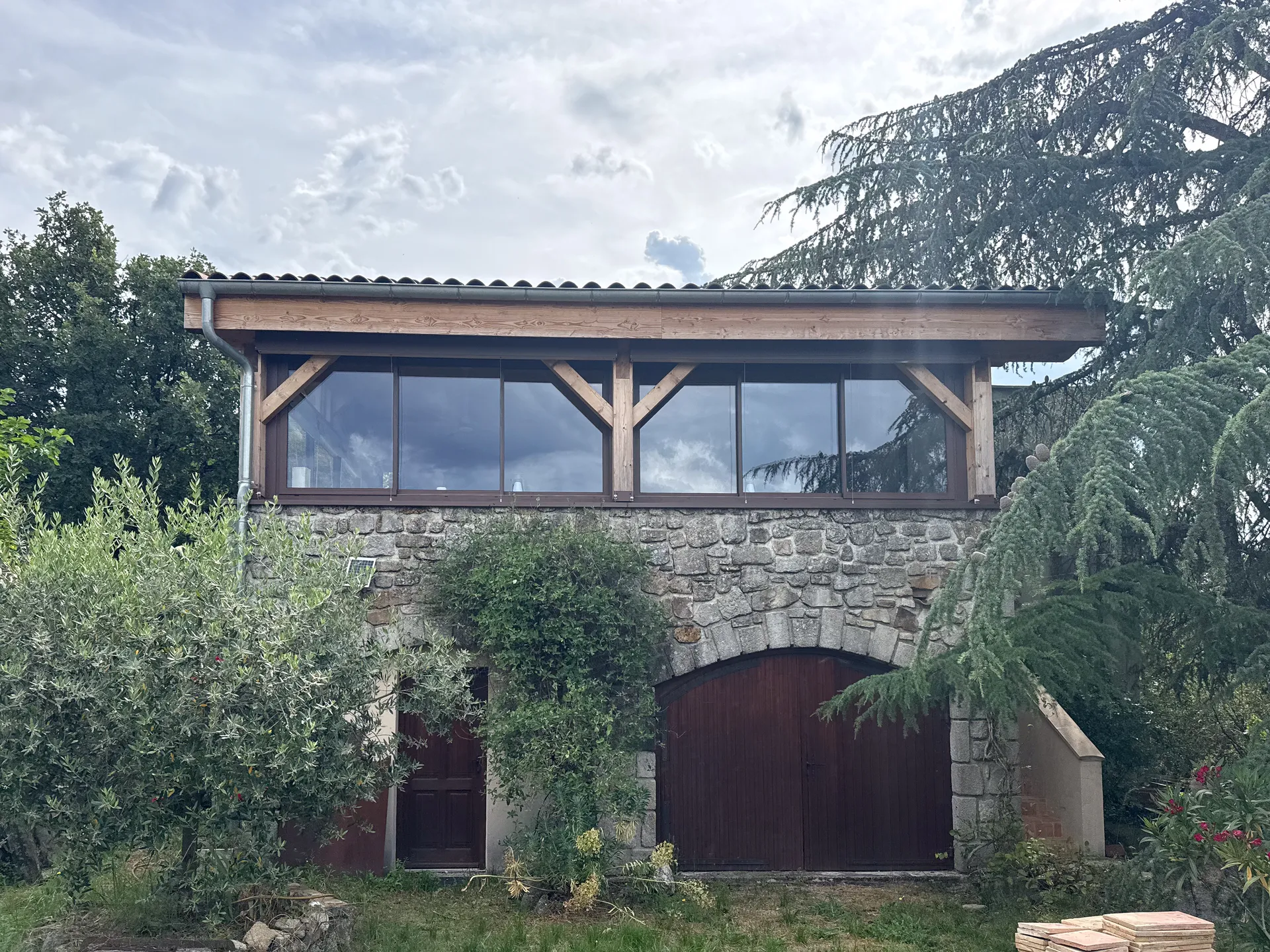 Fermeture d'une terrasse ardéchoise sous charpente bois avec de grands coulissants aluminium teinte rouille