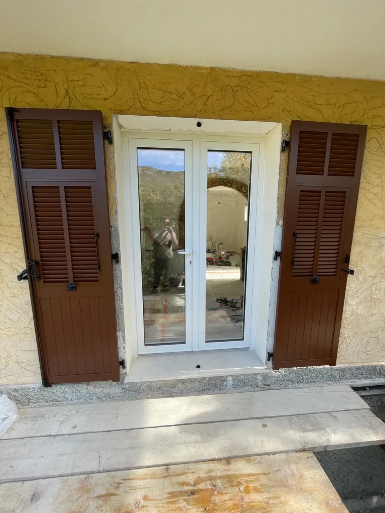 Volets battants aluminium persiennés avec finition RAL 8011S et quincaillerie noire sur maison en rénovation à Contes.