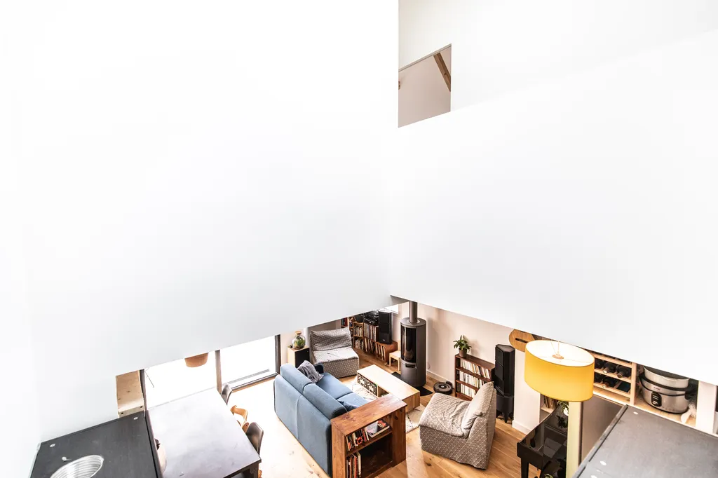 Vue plongeante sur le séjour ouvert  AKIKO ARCHITECTURE – Bègles – Réagencement complet depuis l’étage, la double hauteur dévoile un vaste séjour réinventé : poutres apparentes, volumes blancs et mobilier chaleureux composent un espace fluide entièrement 
