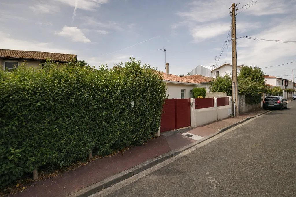 Vue depuis la rue Projet PÊLE-MÊLE au Bouscat : surélévation discrète d’une maison existante, intégrée au tissu pavillonnaire derrière la haie et la clôture sur rue.