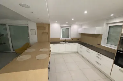 Vue de la cuisine avec le covering de cuisine blanc mat et l'ensemble îlot, retour mural et crédence en adhésif effet bois.