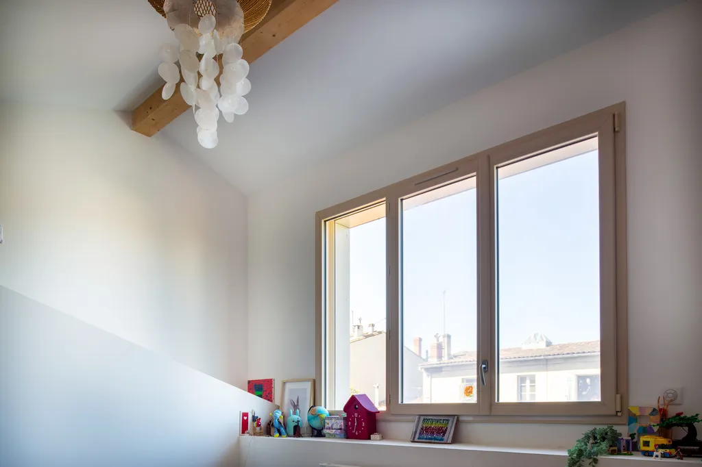 Chambre lumineuse créée lors de la surélévation imaginée par AKIKO ARCHITECTURE dans le quartier Bastide à Bordeaux, mettant en valeur une façade contemporaine sur jardin grâce à une extension de toiture en ossature bois et bardage fibro-ciment