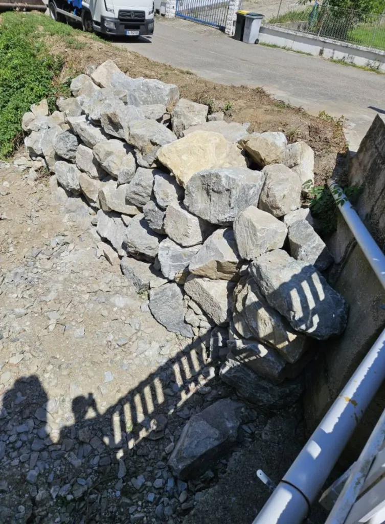Entreprise de terrassement dans l'Ain pour Réalisation d'un enrochement brute avec grosses pierres pour soutenir le mur du fossé à l'entrée d'une maison à Saint-Genis-Pouilly