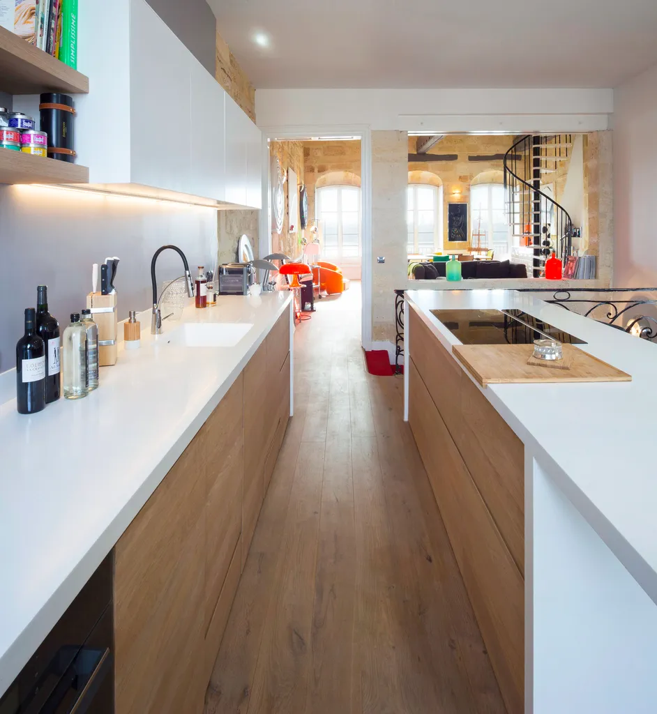 Cuisine traversante & perspective sur le duplex/ Cuisine-îlot sculpturale dessinée par AKIKO ARCHITECTURE, réinventant un duplex en pierre sur le Quai des Chartrons à Bordeaux : une rénovation traversante ouverte vers la Garonne, pensée pour magnifier la 