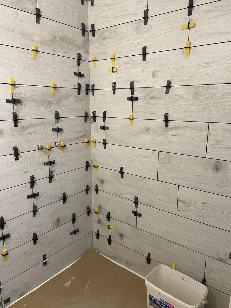 Travaux de second œuvre avec la pose du carrelage mural et de la faïence contemporaine au droit du grand espace douche à l'étage.