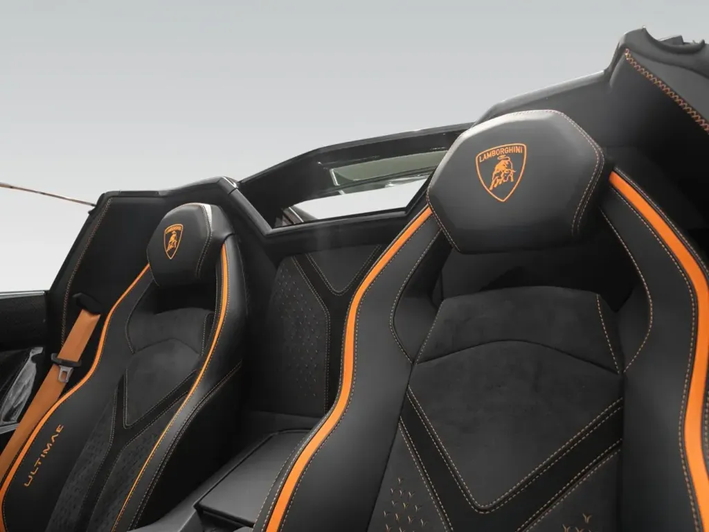 Sièges sport Ultimae en Alcantara et cuir, inserts carbone, broderies Lamborghini et ceintures orange.