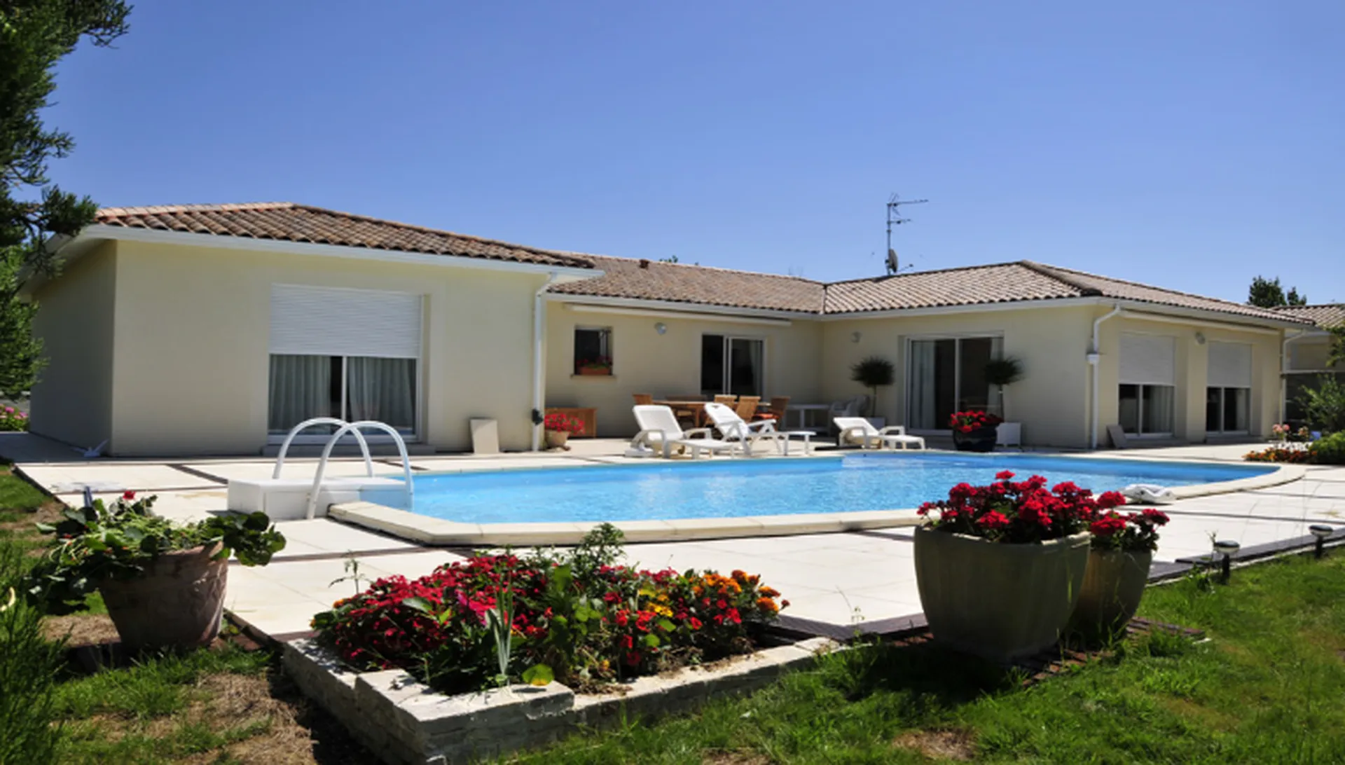 Maison de plain-pied lumineuse en forme de L avec grande terrasse carrelée et piscine, réalisée par Maisons Héraud en Gironde.