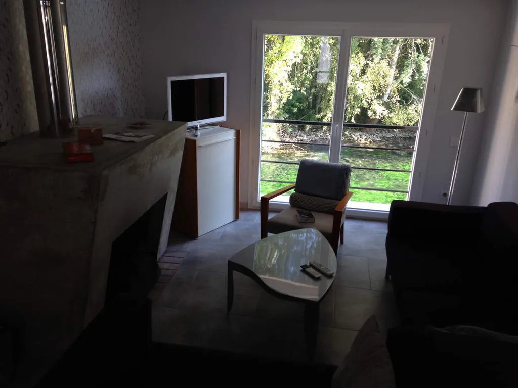 Rénovation d'une maison ancienne au pied de la Sorgue - salon avec sa cheminée en béton et vue sur la Sorgues